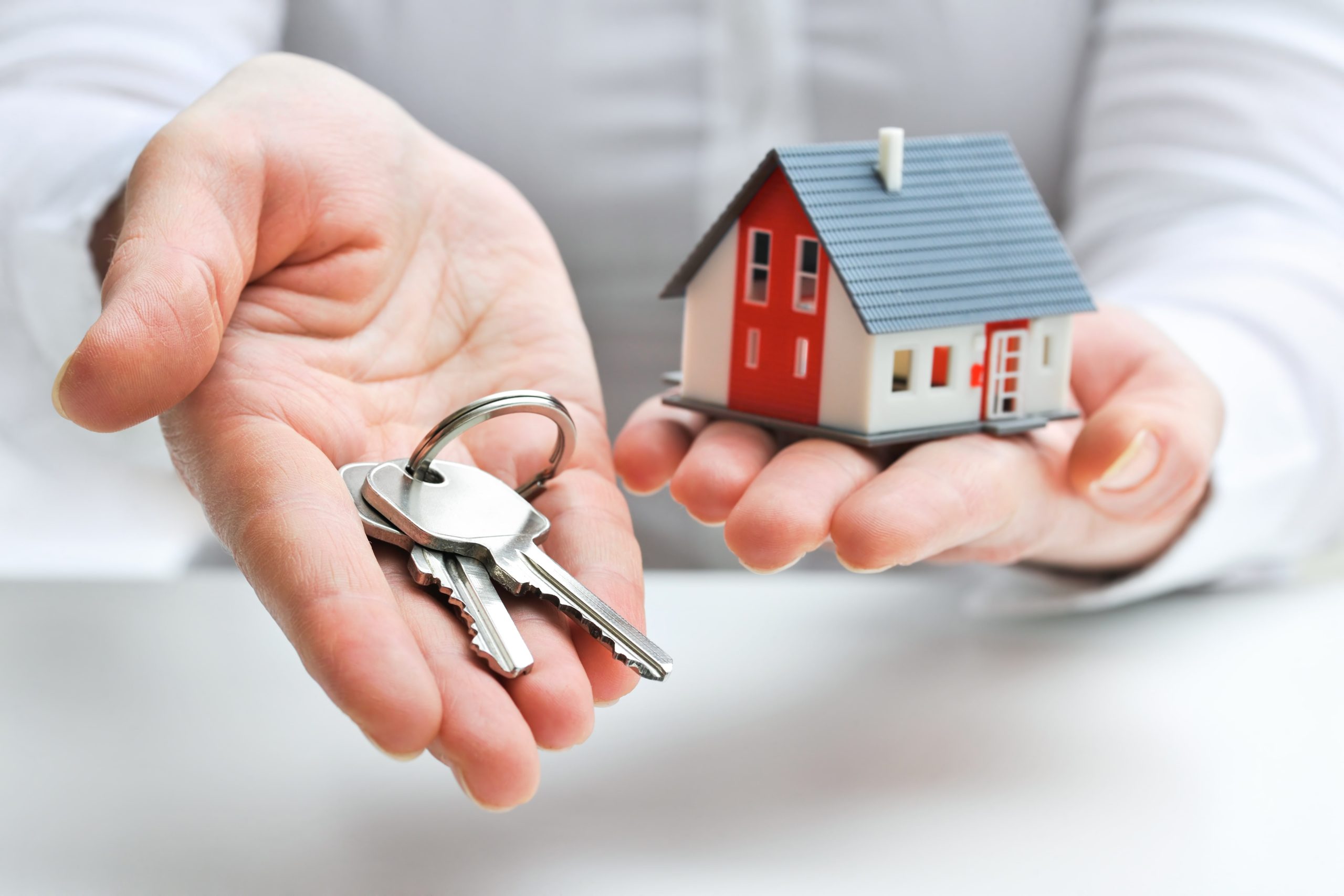 Agent holding house keys in one hand, and a mini house model in the other hand.